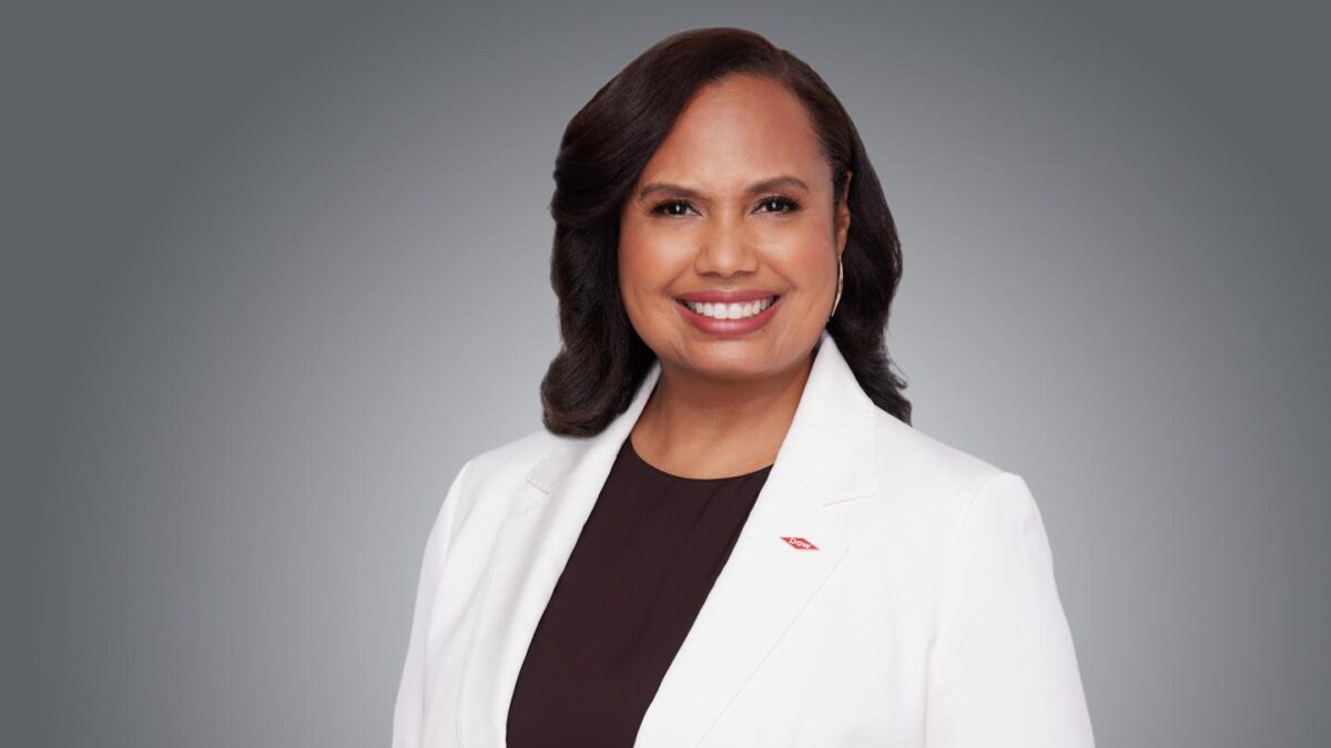 Dow COO Karen Carter wearing a white lab coat and sitting while smiling