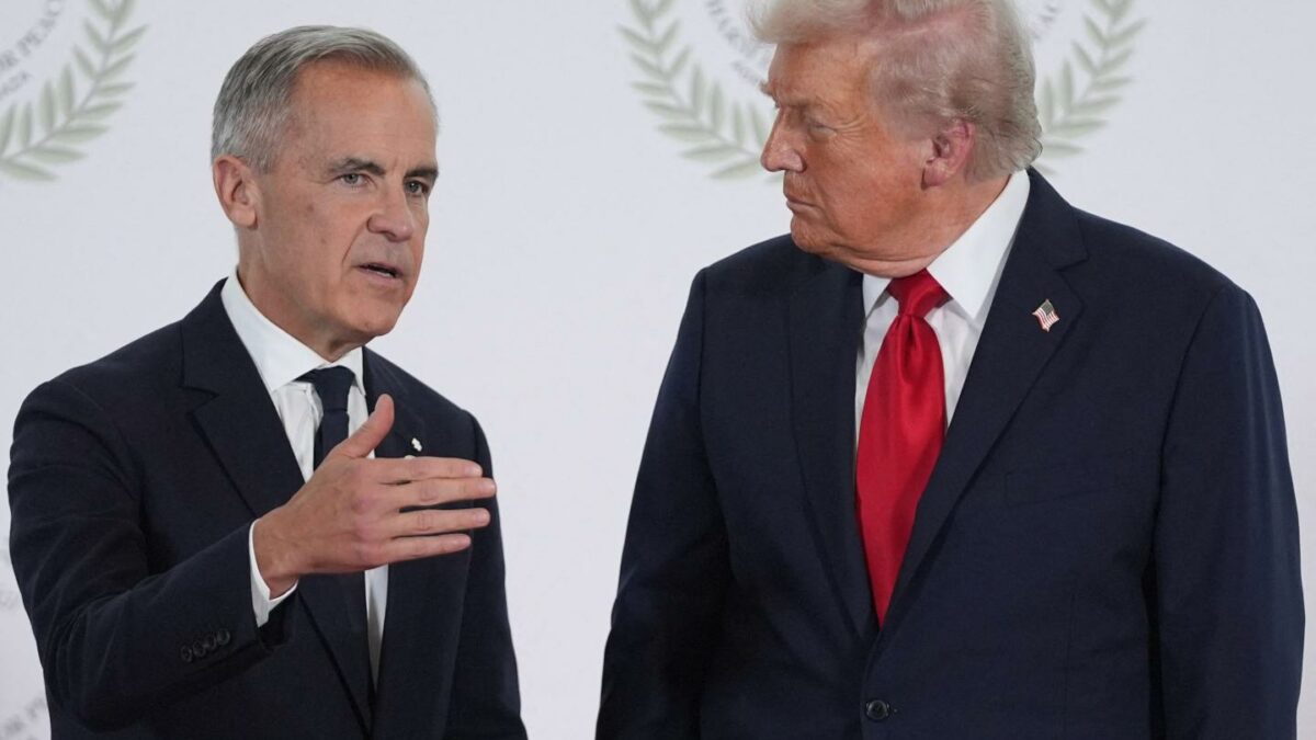 Mark Carney gestures with his hand as he stands next to Donald Trump in front of a white background.