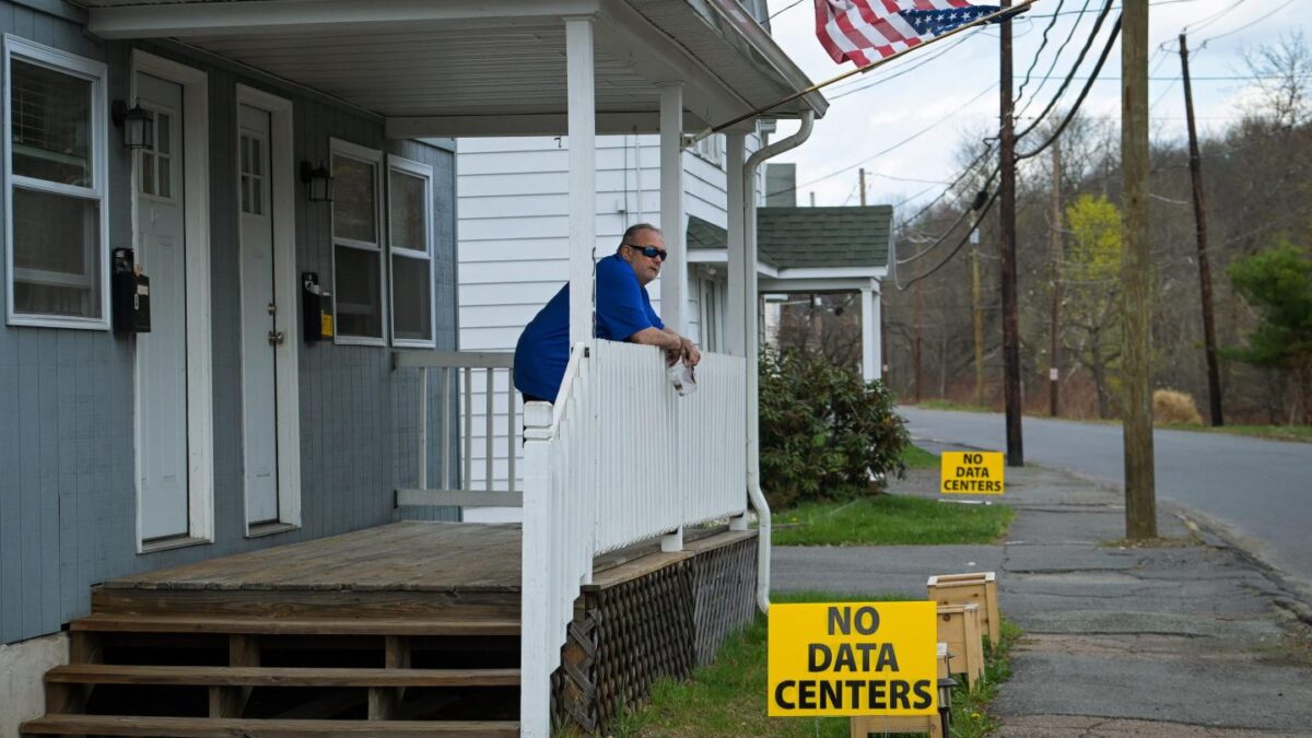 A man stands looking out over his front porch where a sign reads, "No data centers."