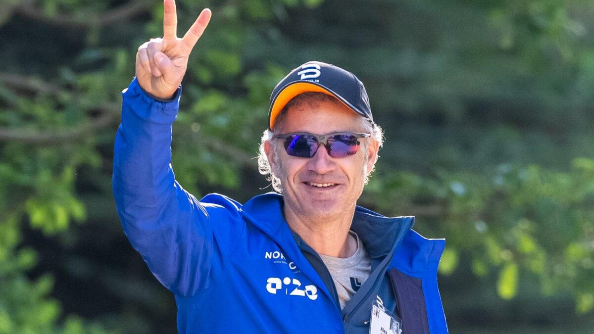 Alex Karp, wearing a hat, gives a peace sign