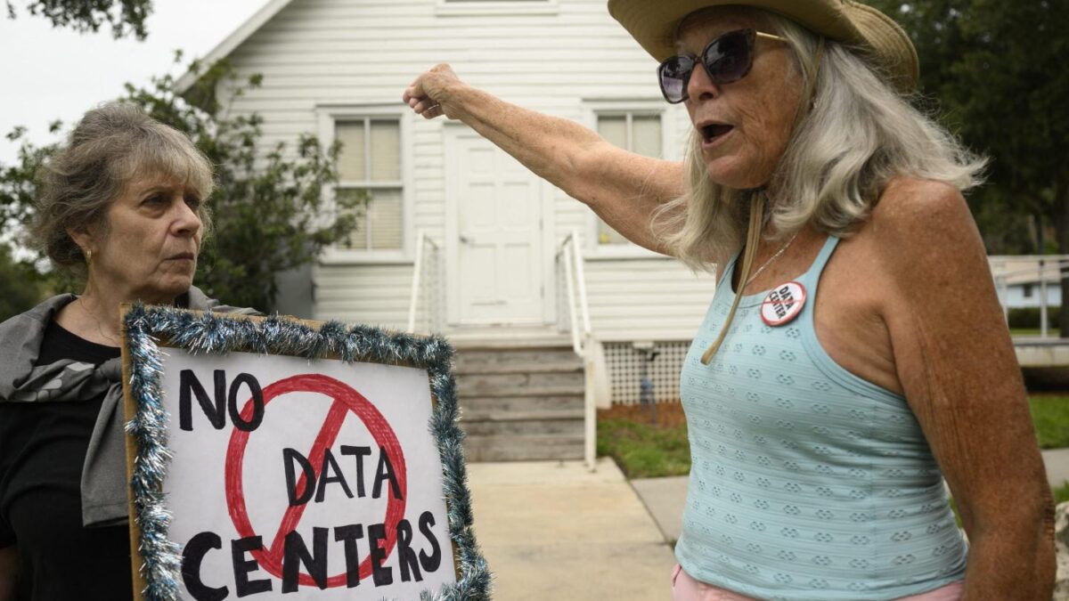 One woman holds a "No data centers" sign while another points toward a white house.