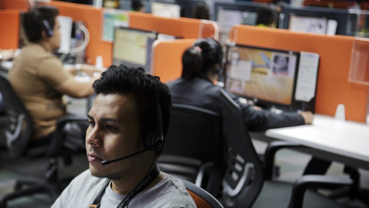A man with a headset sits at a desk in a call center.