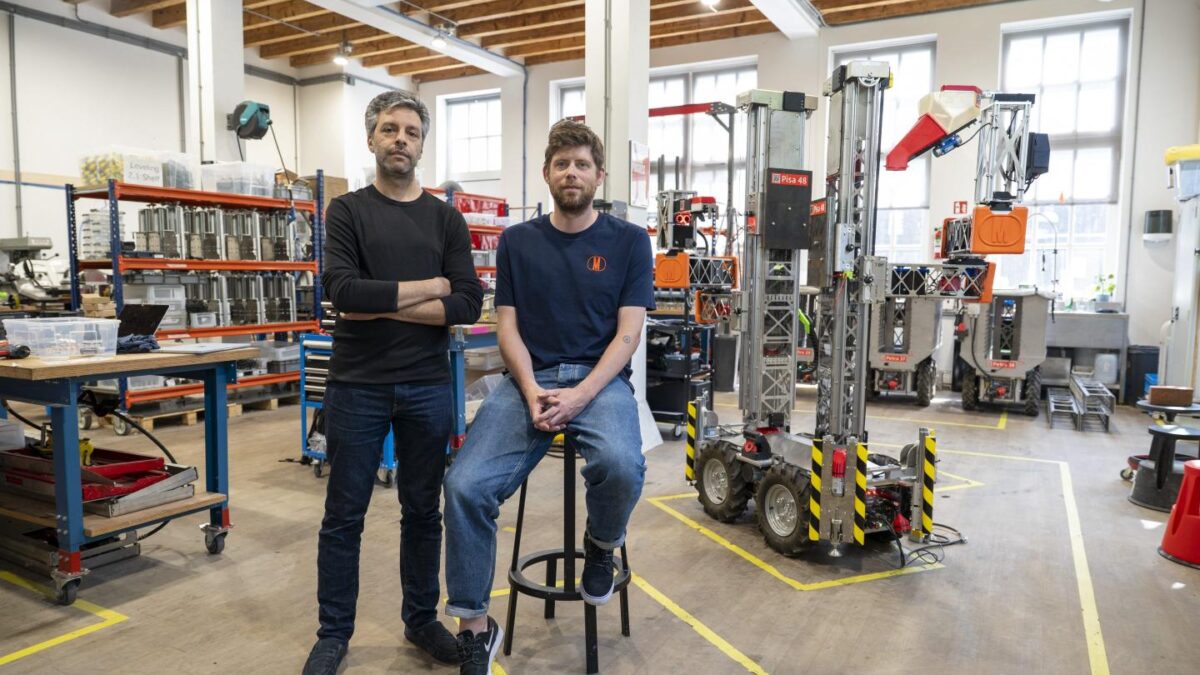 Salar al Khafaji stands while Sebastiaan Visser sits on a stool in front of a robotics warehouse